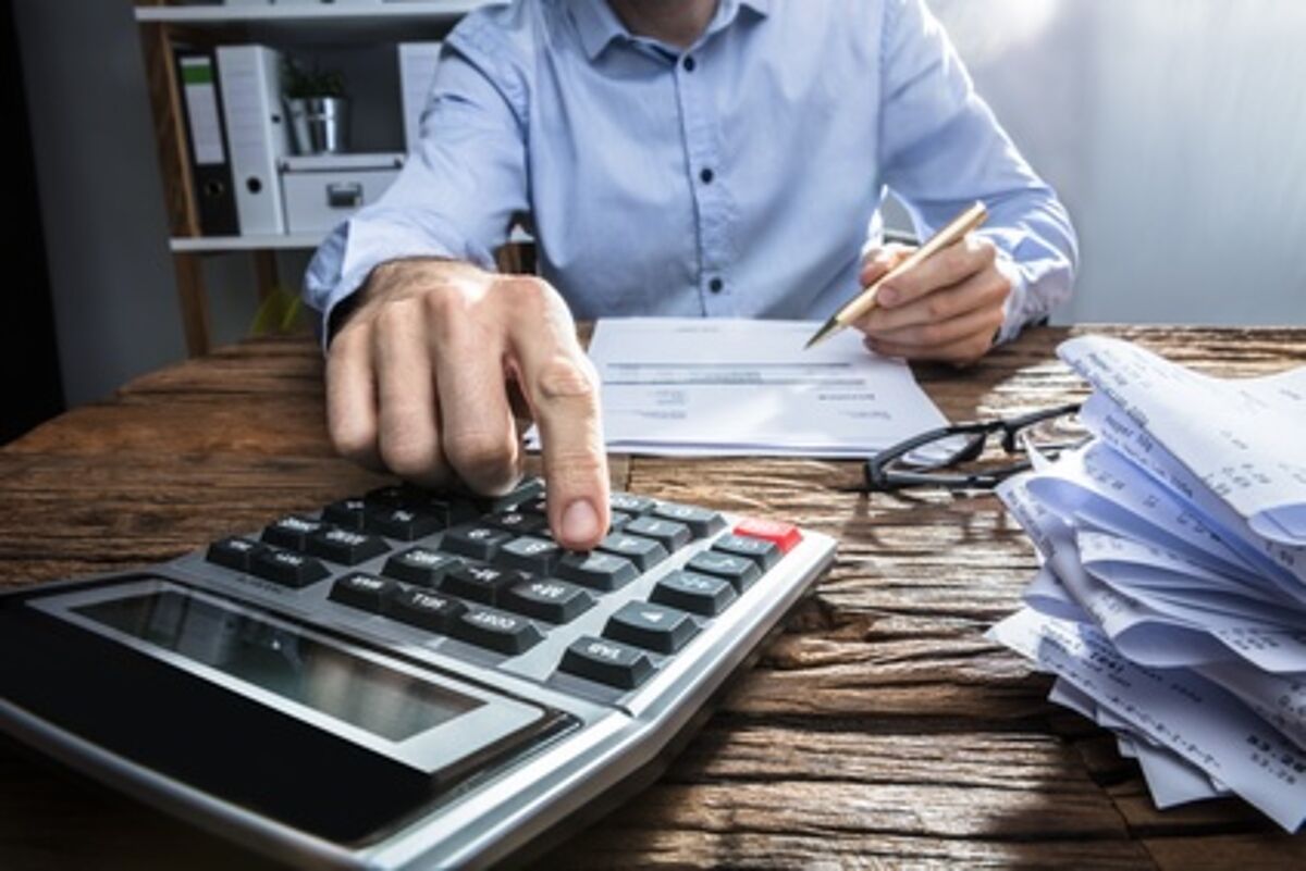Close-up Of A Businessperson's Hand Calculating Invoice With Calculator At Workplace